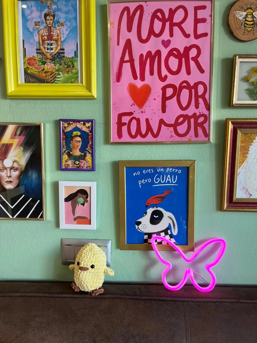Pared del estudio llena de cuadros, con un cartel de «More amor por favor» y una mariposa de neón