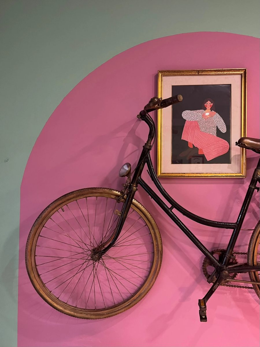 Bicicleta antigua colgada sobre el arco rosa del estudio, junto a una lámina enmarcada