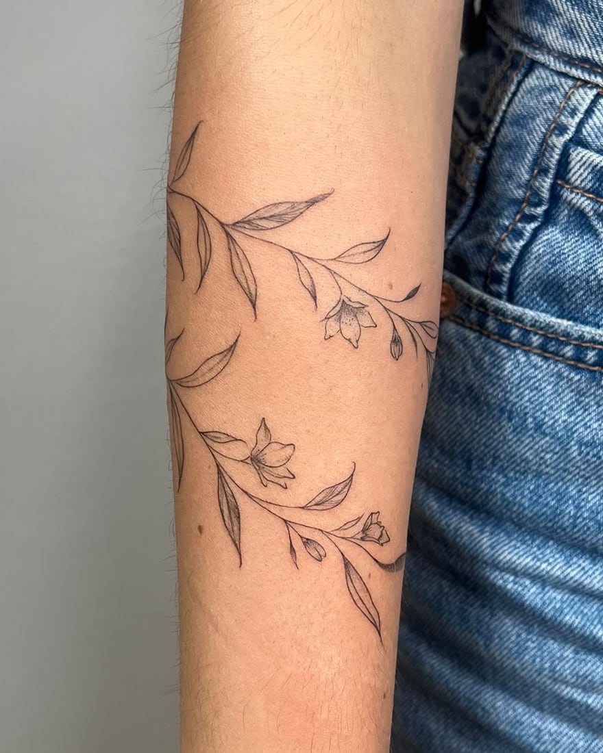 Enredadera de hojas y flores en línea fina rodeando el antebrazo
