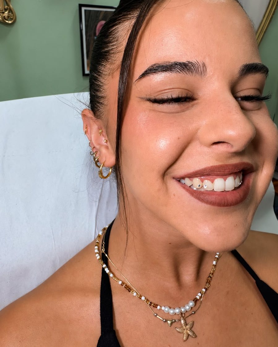Chica sonriendo con dos gemas dentales y piercings en la oreja