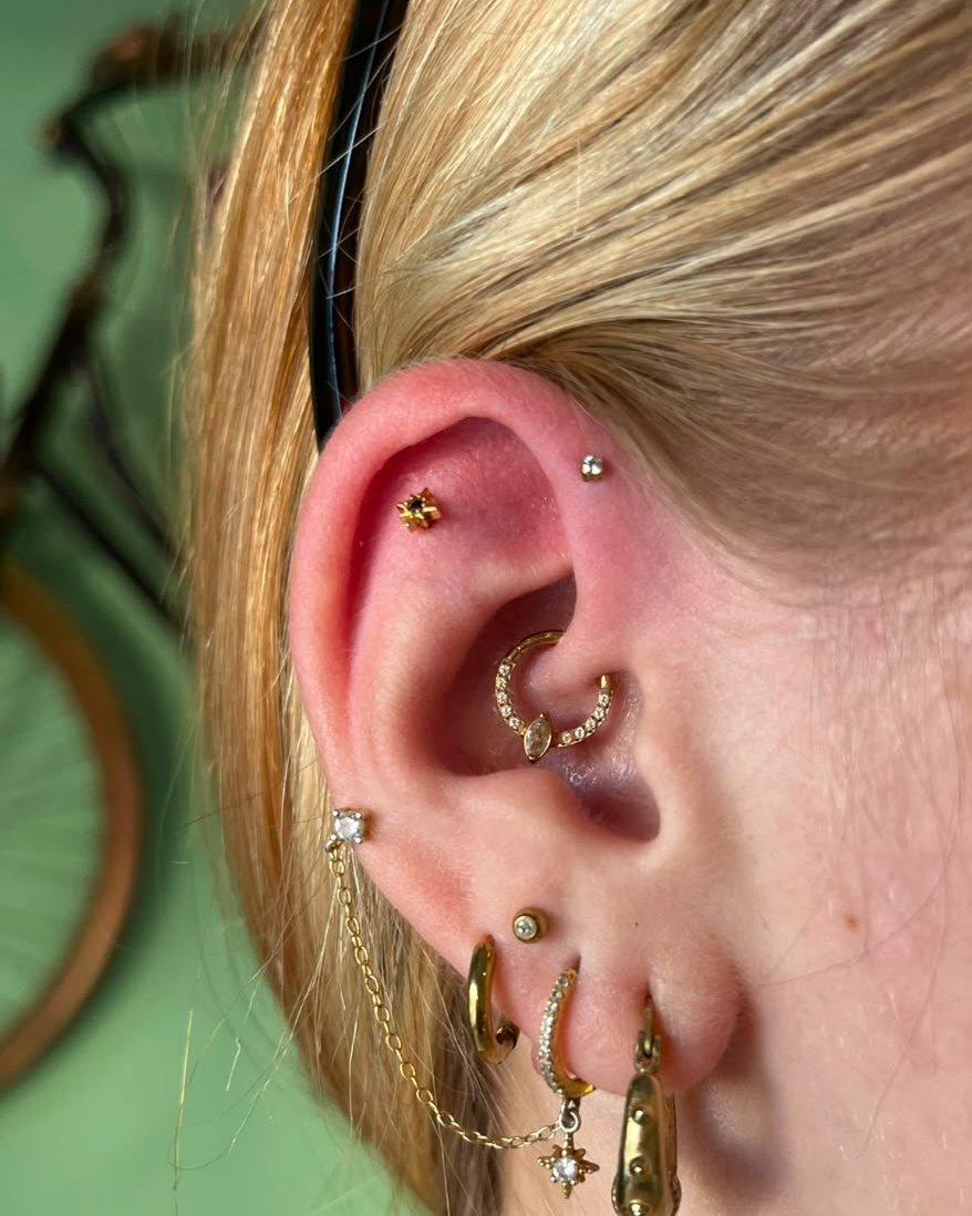 Oreja con piercing de daith con brillantes, cadena y varios aros dorados